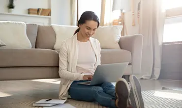 woman sitting by couch and typing on laptop